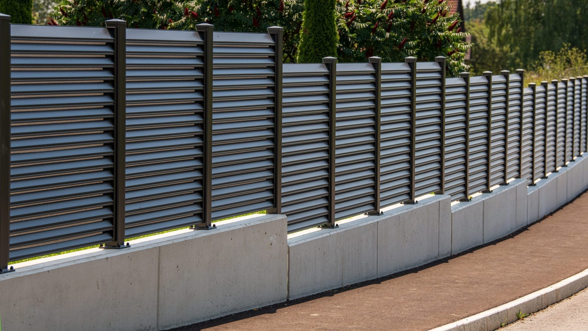 Aluminum privacy fence along a street with a garden behind, showcasing commercial fencing solutions Jacksonville.